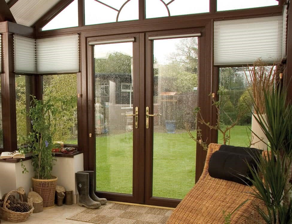 Brown French patio doors with gold handles leading from conservatory to gassy garden